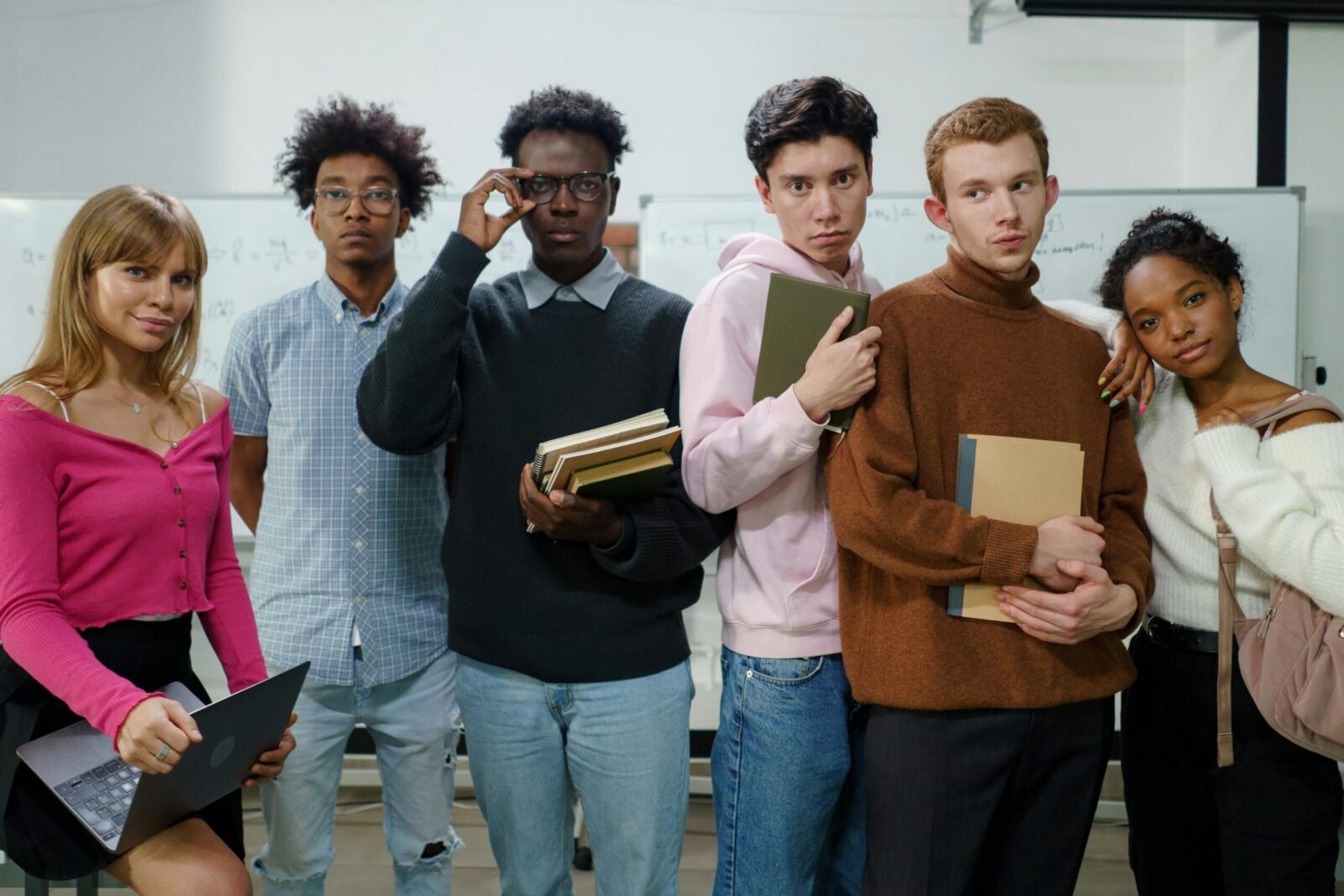A group of diverse college students posing with books and devices indoors.