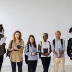 Group of diverse young multiracial classmates with notebooks and textbooks and backpacks smiling at camera