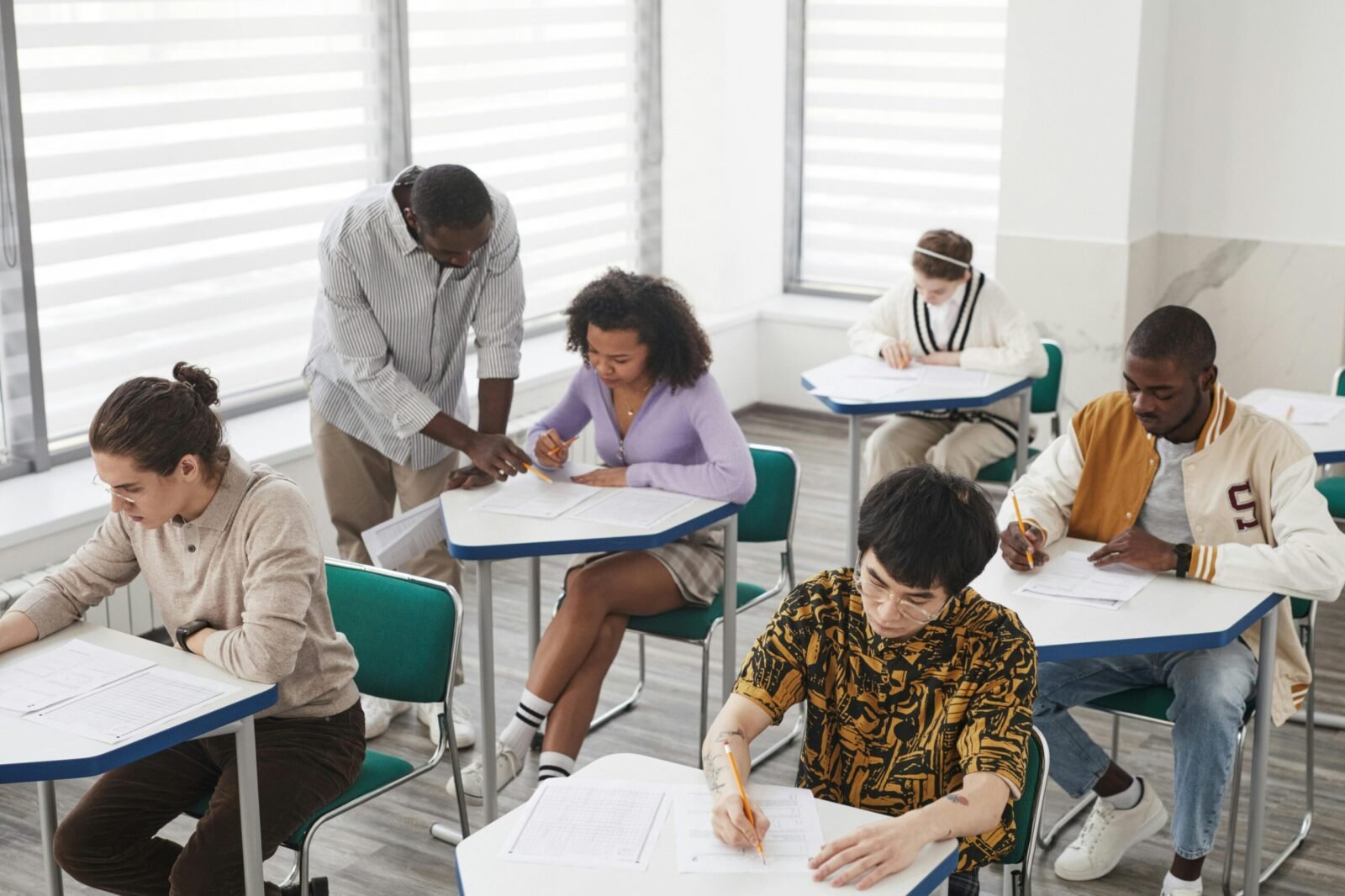 A diverse group of college students taking an exam, supervised by a teacher, in a classroom setting.