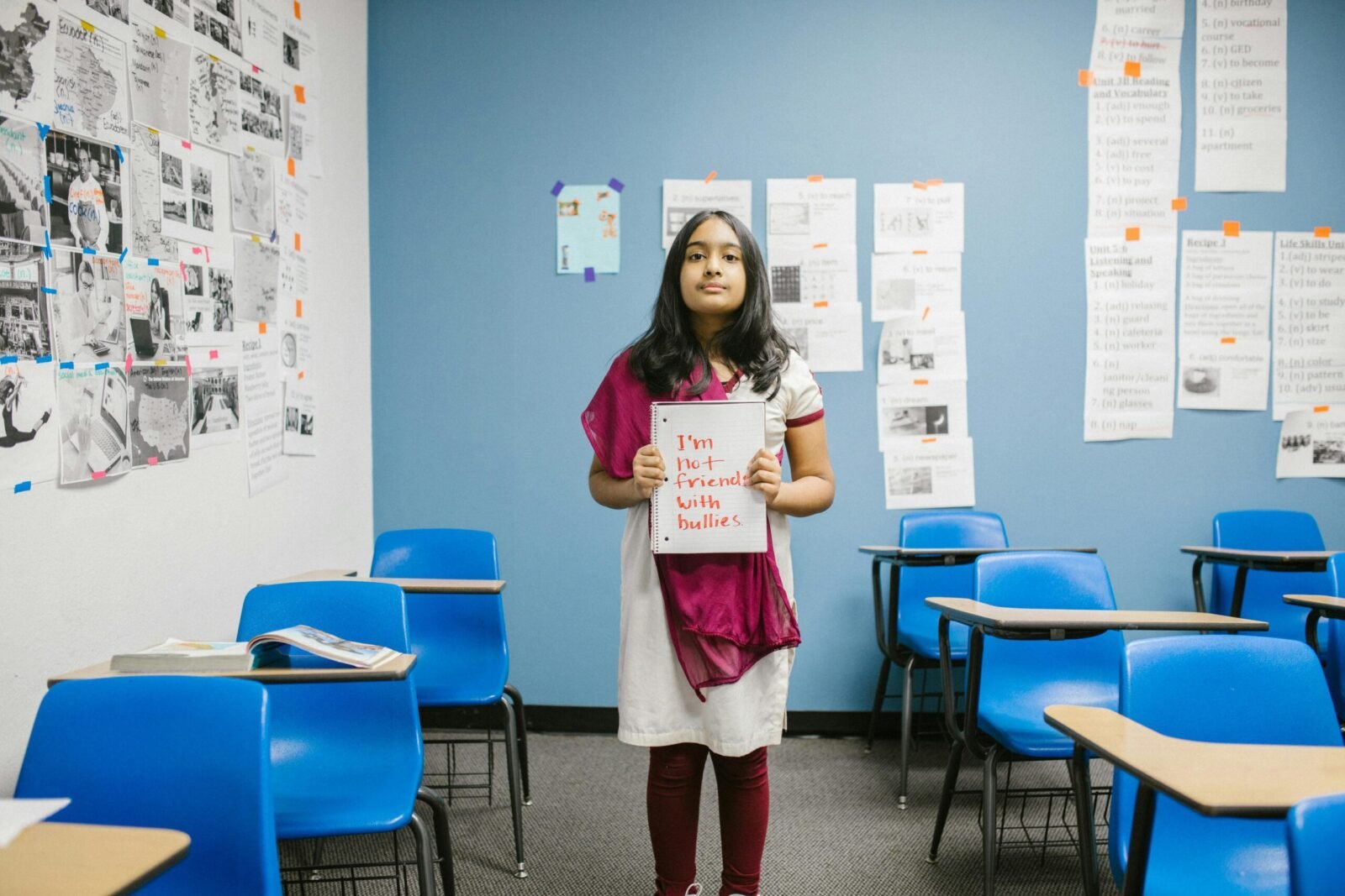 A young girl holding a sign promoting anti-bullying in an empty classroom, emphasizing awareness.